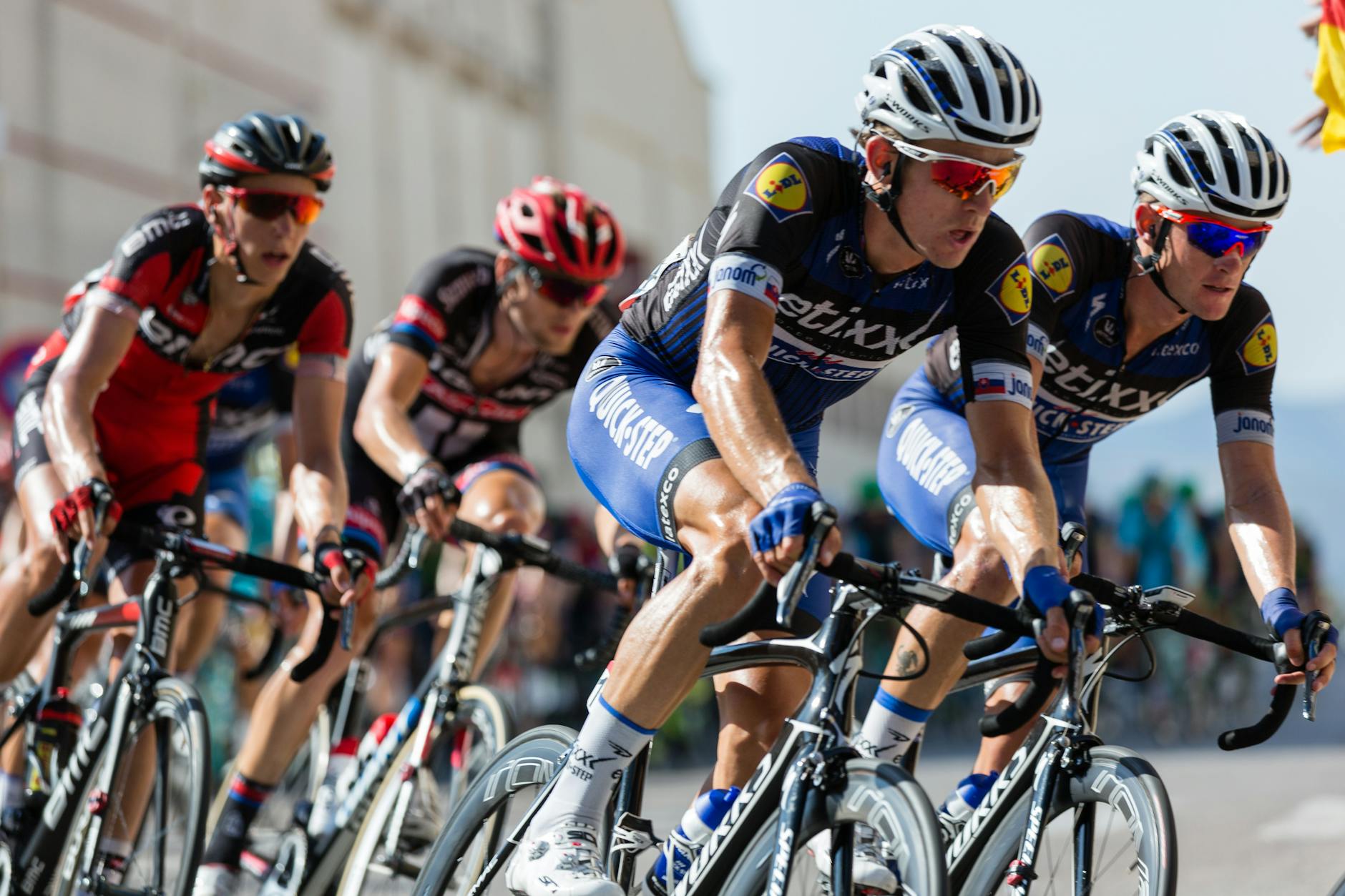 Um grupo de cinco ciclistas competindo em alta velocidade em uma curva apertada de um circuito, com um foco na primeira fila. Eles estão bem alinhados, com posturas aerodinâmicas, transmitindo a intensidade da competição. 