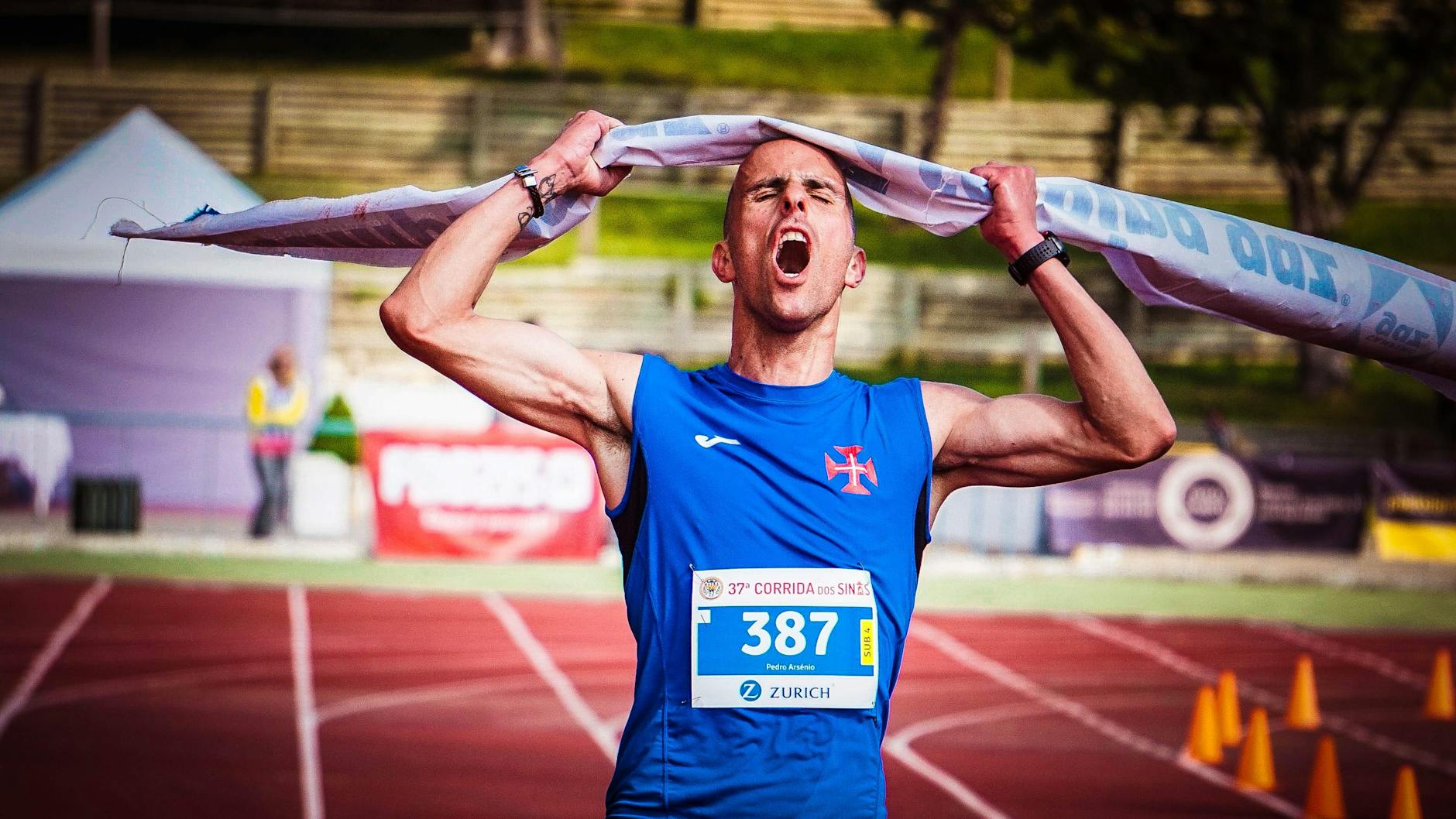 Homem comemorando sua chegada na linha de chegada de uma corrida, com um sorriso de conquista e braços erguidos, simbolizando a celebração da sua alta performance esportiva.