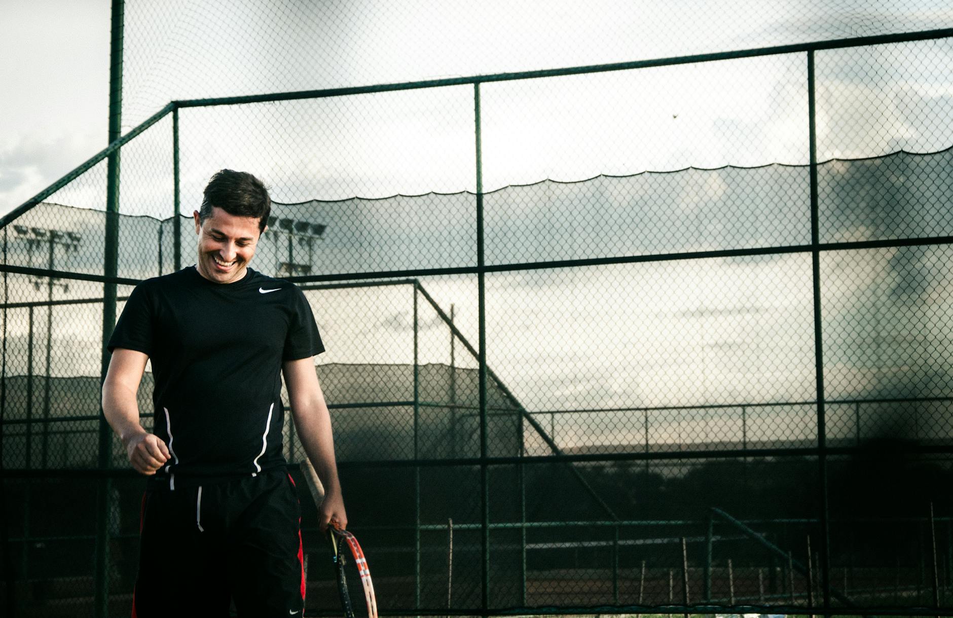 Jogador de beisebol saindo do treino, sorrindo e com expressão de satisfação, cheio de autoconfiança, sabendo que deu o seu melhor durante a sessão e indo em direção ao próximo desafio fora do centro de treinamento.