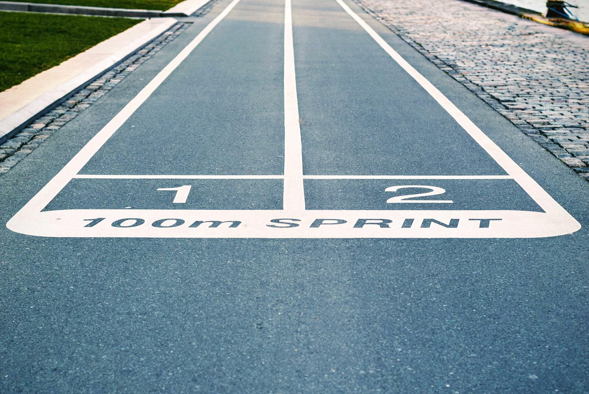 A imagem mostra o início de uma pista de atletismo de 100m sprint, com as linhas 1 e 2 marcadas no chão, indicando o ponto de partida para os atletas.