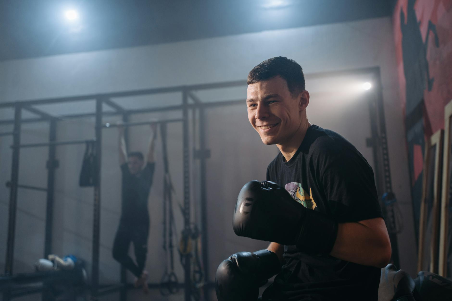 Atleta sentado na academia, com luvas de boxe nas mãos e um sorriso de satisfação, celebrando o treino realizado com foco e preparação mental.