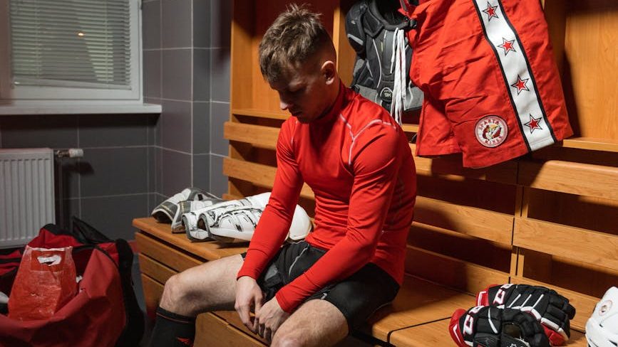 Jogador de hóquei no vestiário, vestido com seu uniforme vermelho, praticando a visualização positiva para controlar a ansiedade e entrar em campo com confiança e foco no desempenho.