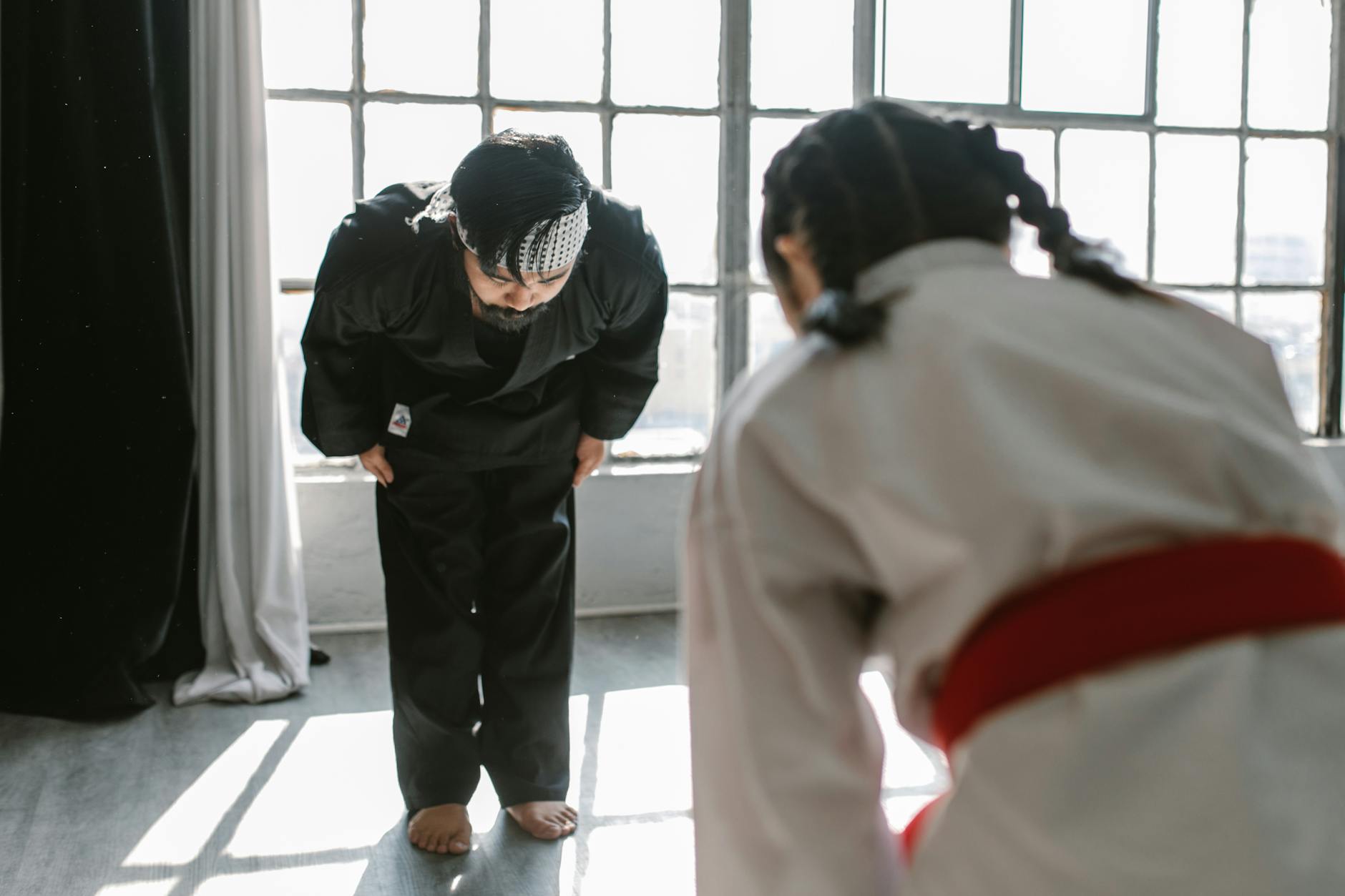 Um sensei e sua aluna se cumprimentam com uma reverência respeitosa, valorizando o momento de aprendizado na academia, em um ambiente de foco e tranquilidade, livre de ansiedade ou estresse.
