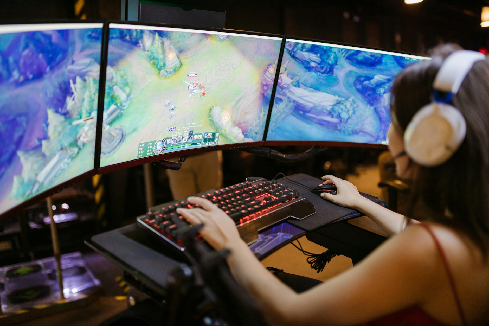 Uma mulher jogando jogos eletrônicos, completamente imersa na experiência, com três monitores à sua frente exibindo cenas do jogo. Ela está concentrada, segurando o mouse e o teclado com firmeza, demonstrando controle e estratégia no ambiente competitivo de eSports